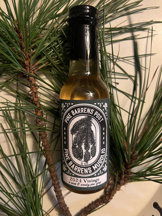 A bottle of Pine Barrens Pine Syrup (Mugolio) placed among pine needles.